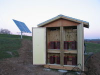 Battery side of the shed. The dump load resistors are visible in the upper part of the shed. Off to the left is the poly tubing and burried wire that goes back to the dorm.