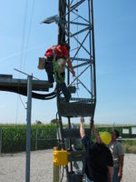A Tower Tech employee has attached the 10 watt solar panel to the tower and is about to install the 900 MHz yagi antenna. The solar panel powers the wind data logging equipment. The antenna is used to send the live data to the owner's house about 1000 feet away.