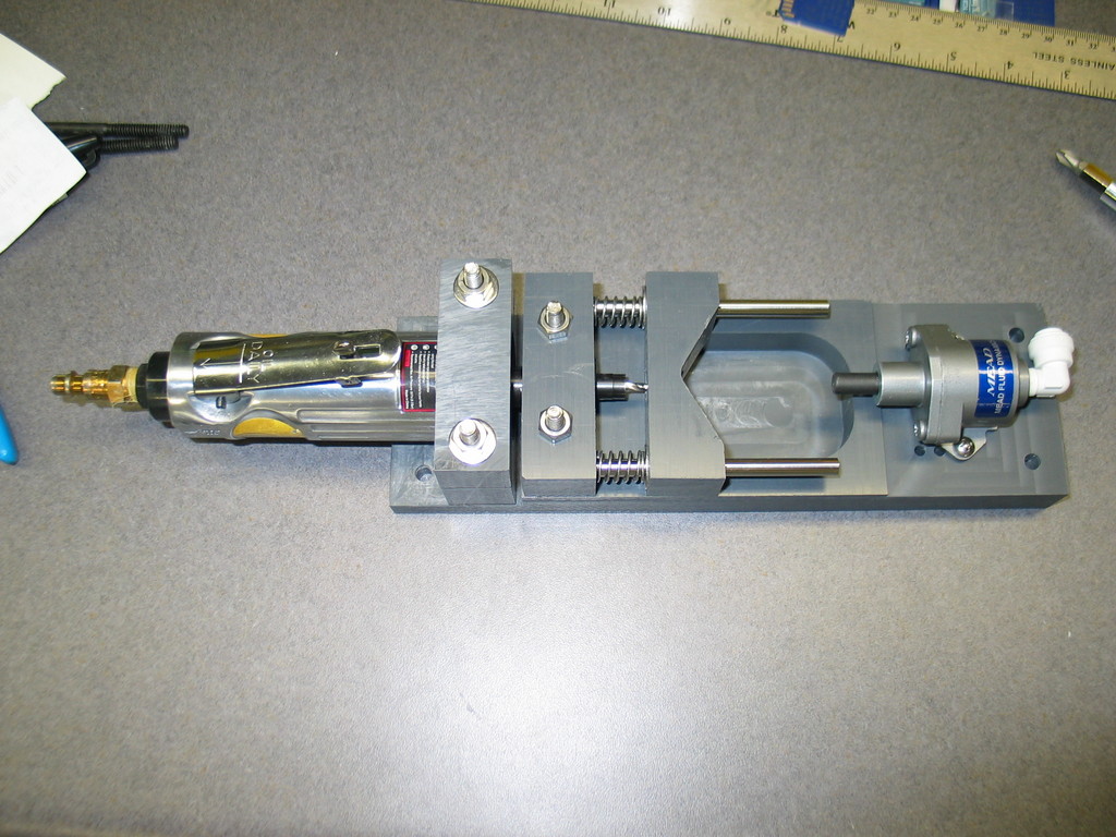 Pneumatic PVC drill. The air cylinder on the left pushes the PVC pipe into the v-block. The springs behind the v-block compress and the PVC pipe feeds into the 22,000 RPM drill bit. Instant perfectly aligned hole.