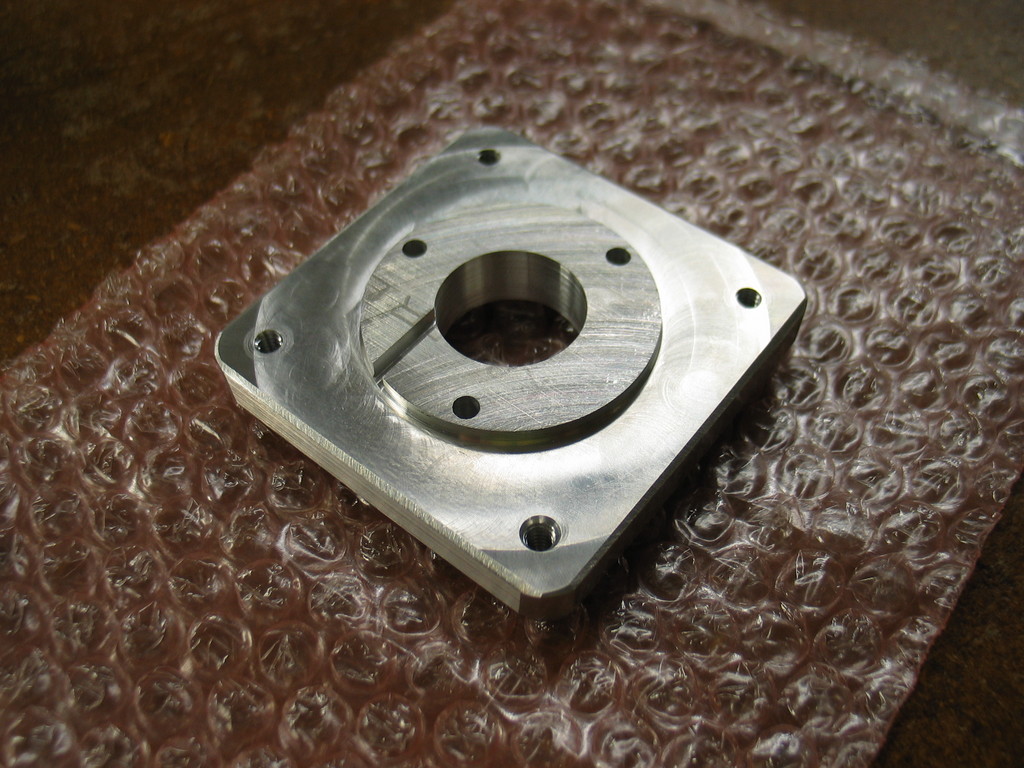 Adapter plate for attaching encoder to motor gear box. The slot is to allow an allen wrench in to tighten the clamp screw on the coupler to the encoder shaft.