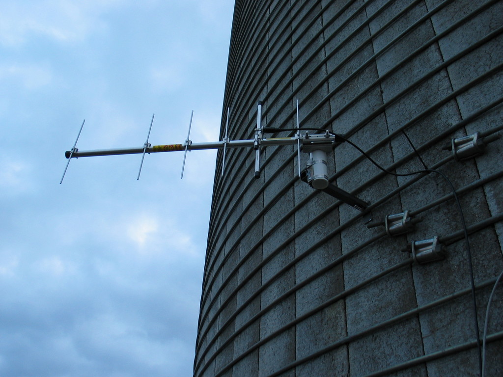 Example bracket for mounting an antenna or anemometer to a silo band. This was created in a few minutes by welding some scrap 1" square tubing, plate, and the u-bracket. 1.5" PVC pipe is hose clamped into the bracket. That could be an anemometer, wind vane, or tee.